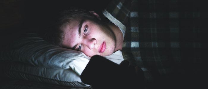 A picture of a young man lying on his side in bed while looking at his phone