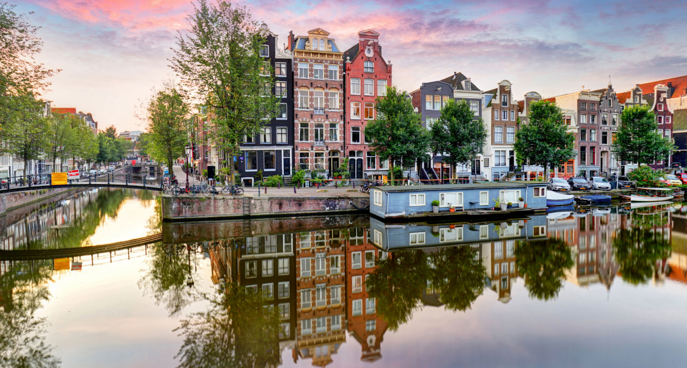 Narrow houses and boathouses reflecting in the water of a canal, Amsterdam [Photo: Shutterstock]