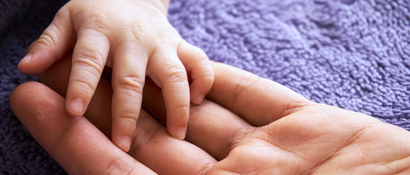 Photo of baby and parent holding hands with purple background