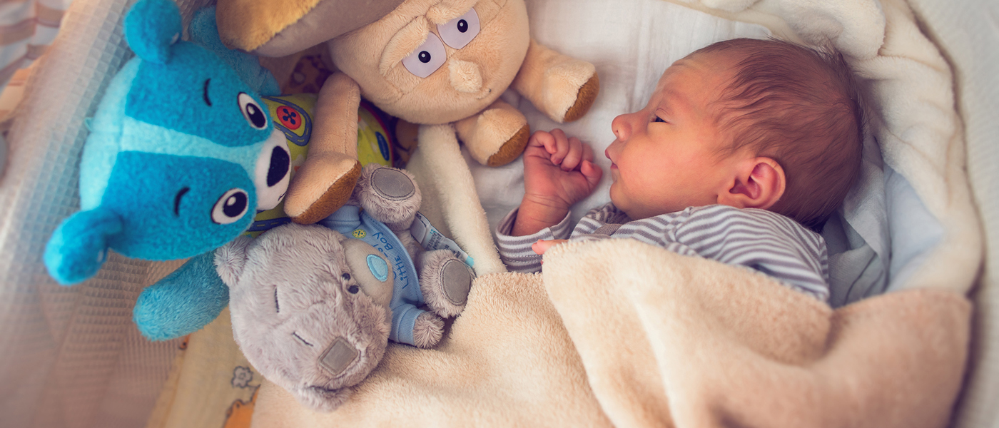 Photo of newborn baby in cot with toys