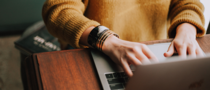 A person wearing a yellow jumper with their hand typing on a keyboard