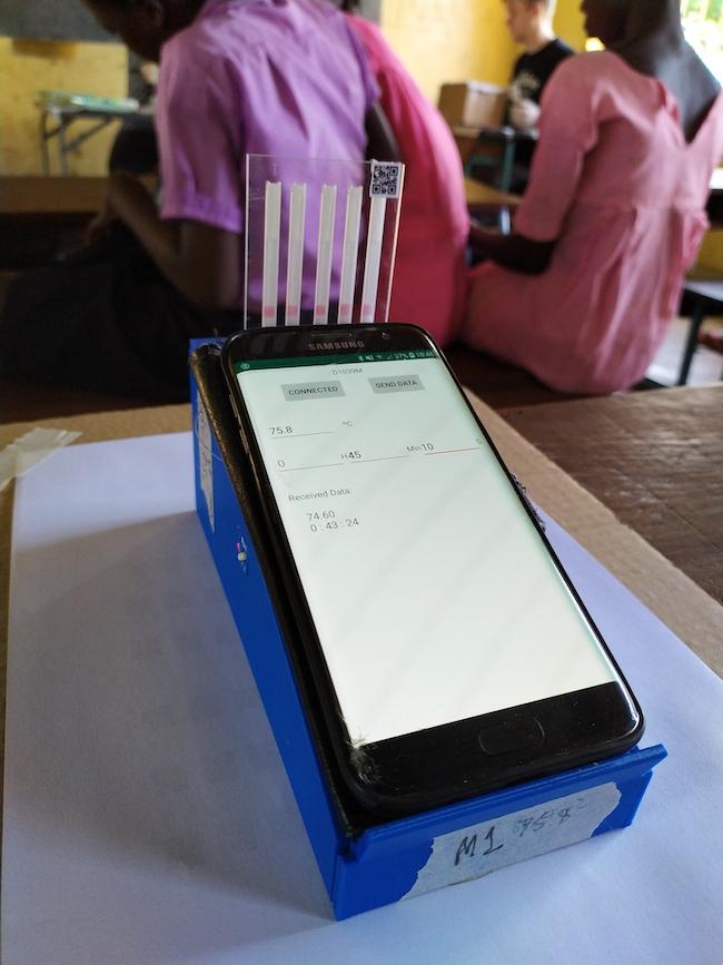 A smartphone running the origami diagnostic system app sits on a table in a Ugandan classroom