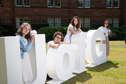 UofG Letters and Students leaning on them 