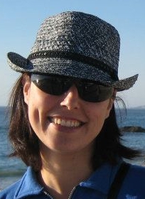 Picture of her face with glasses and a hat, by the sea.