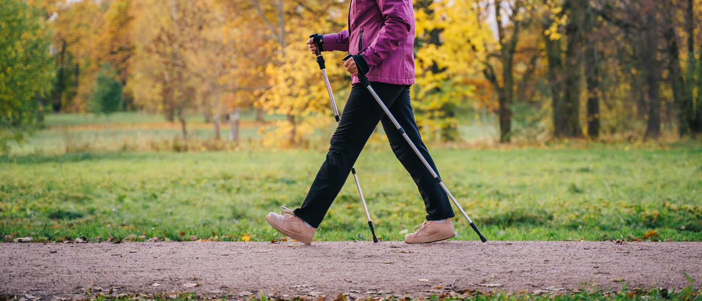 Photo of older woman walking in a park with poles 