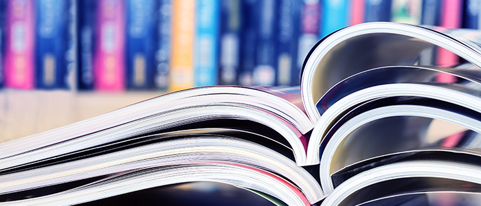 close up stacking of opened magazine with blurry bookshelf background , extremely shallow DOF