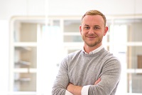 Dr Andrew Struan - he is smiling at the camera, wearing a white shirt and beige jumper and has his arms folded.