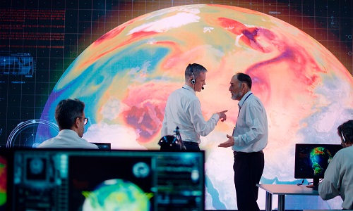 A younger man and an older man in front of a warming globe, discussing