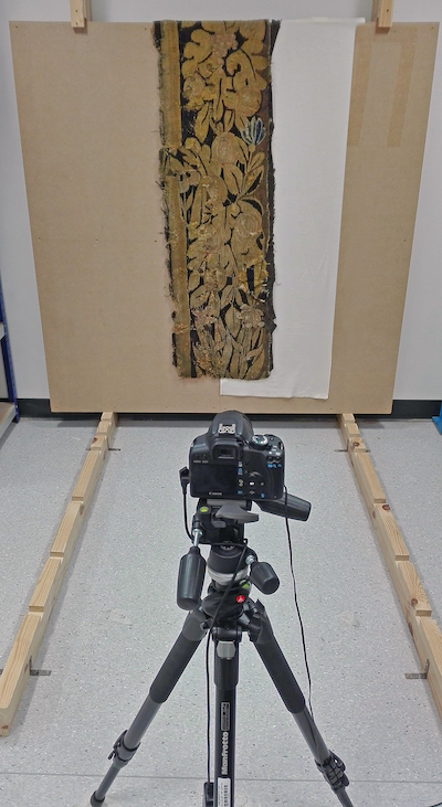 A small tapestry suspended against a vertical board, half-covered with a cotton molton fabric. © University of Glasgow