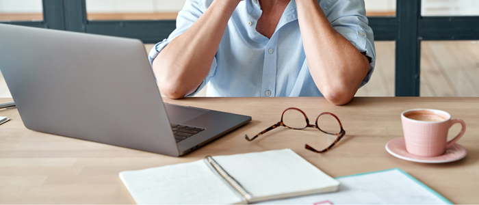 Photo of overworked person working on laptop with coffee, glasses and notepad