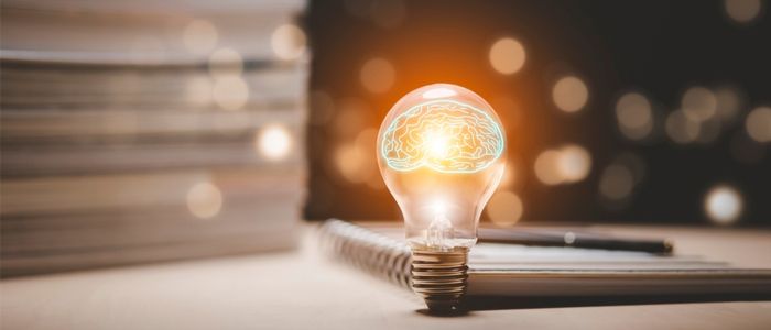 Image of a light bulb in front of a stack of notebooks