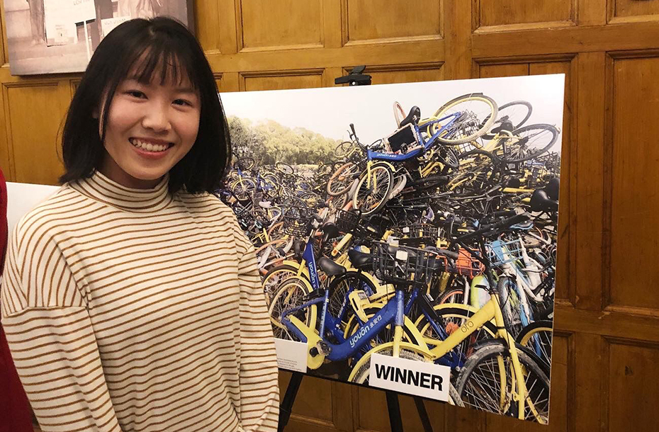 Xin Ning standing by her winning photograph of a pile of bicycles