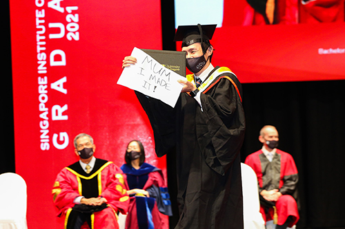 Singapore Institute of Technology graduate on the stage holding a sig saying 