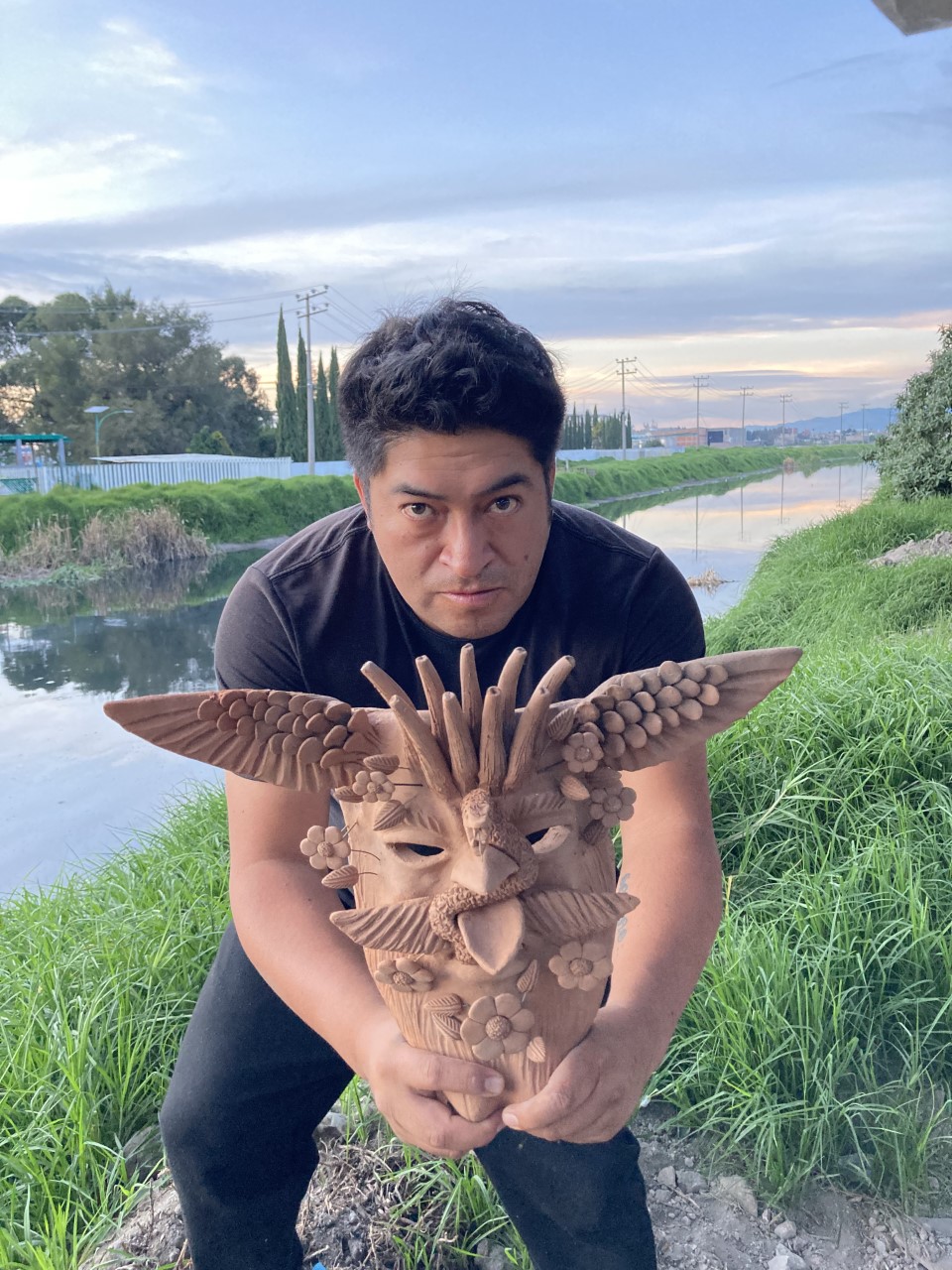 Man crouching with Mexican indigenous mask by river