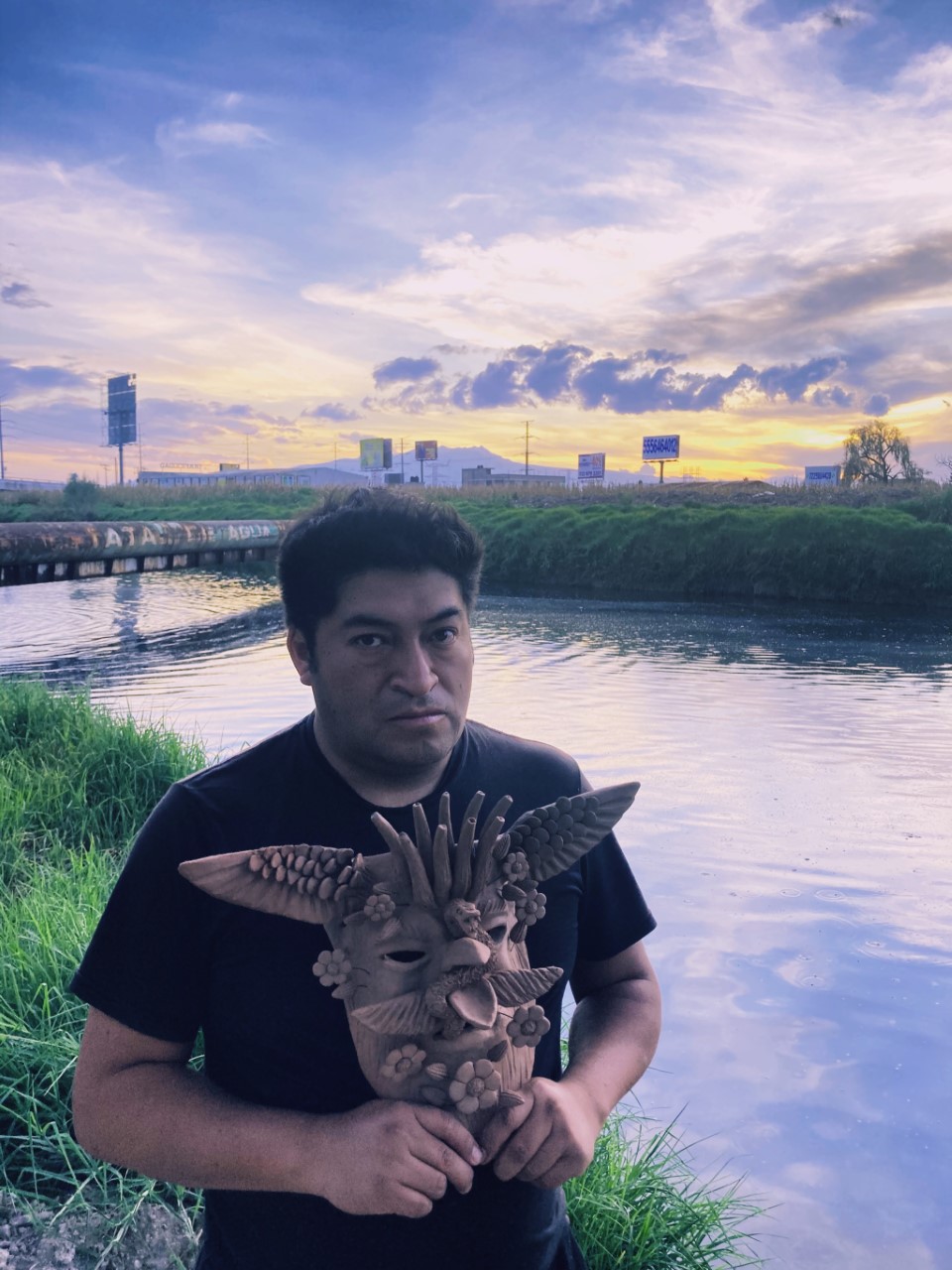 Man holding Mexican indigenous mask by river at dusk
