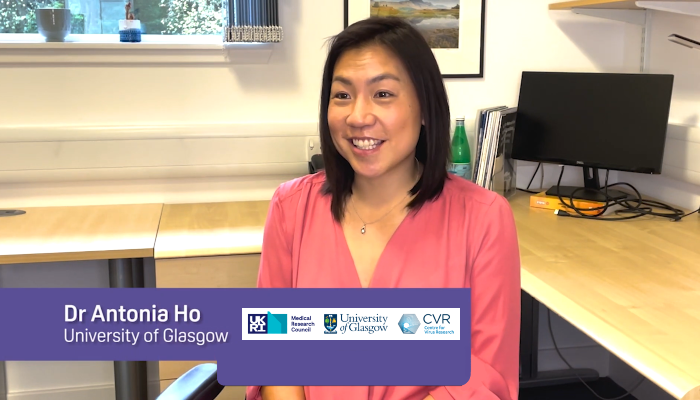 Dr Antonia Ho sat at a desk during a video interview with caption showing her name and the institution logo