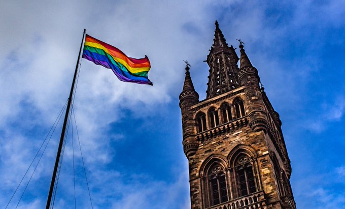 The low angled image of a LGBTQ+ flag on the pole outside UofG main tower