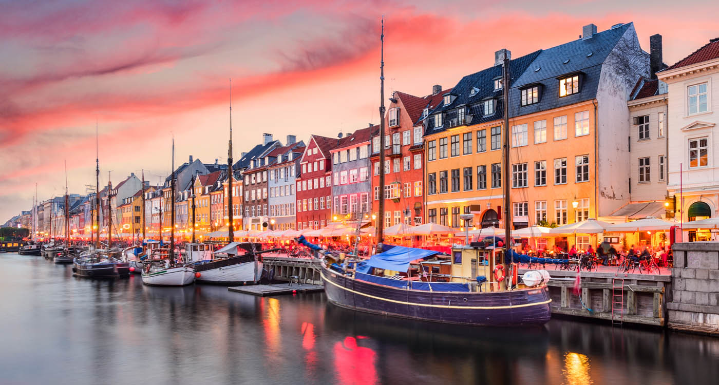 Row of colourful buildings in sunset alongside the Nyhavn Canal, with boats lined along the side of the canal [Photo: Shutterstock]