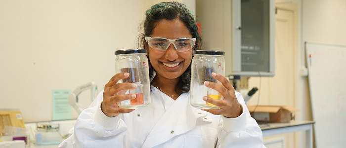 A student in the lab holding jars with experiments inside