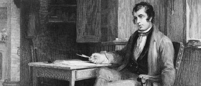 Robert Burns sitting a his desk with a quill in his hand. 