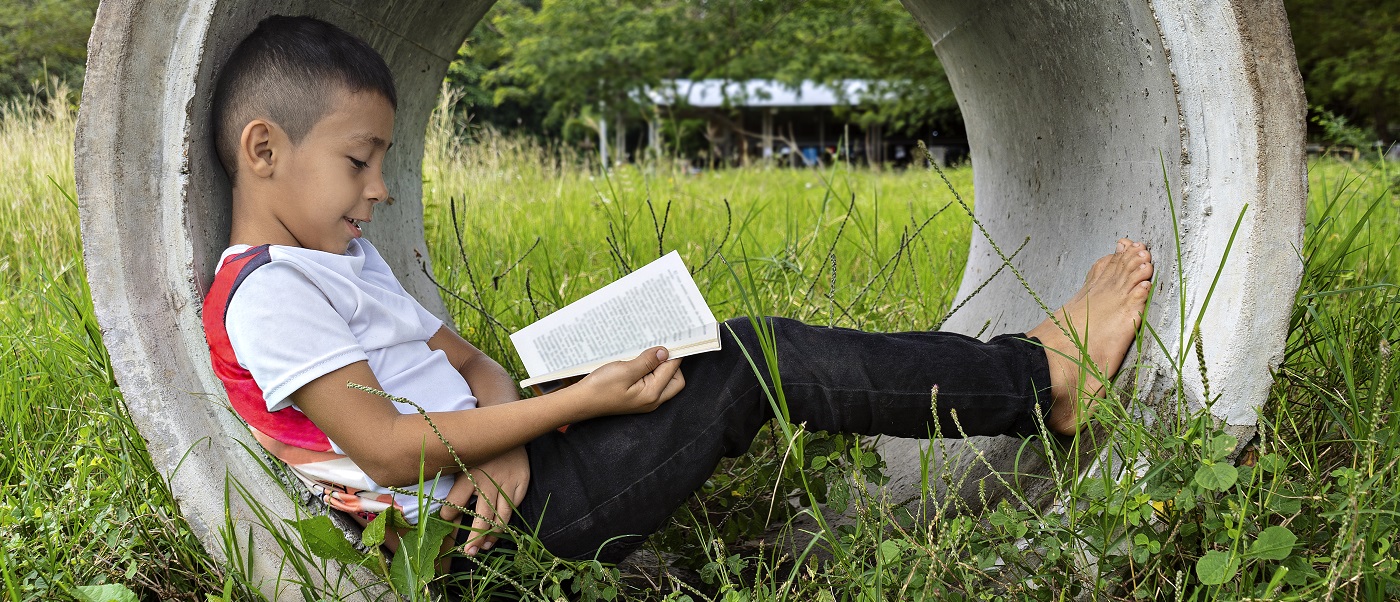 A boy lying inside a concrete pipe in a field and reading a book. Image credit: RECVISUAL | iStockphoto https://www.istockphoto.com/photo/boy-reading-a-book-sitting-on-a-concrete-pipe-on-a-sidewalk-very-happy-and-smiling-gm1295650597-389311729