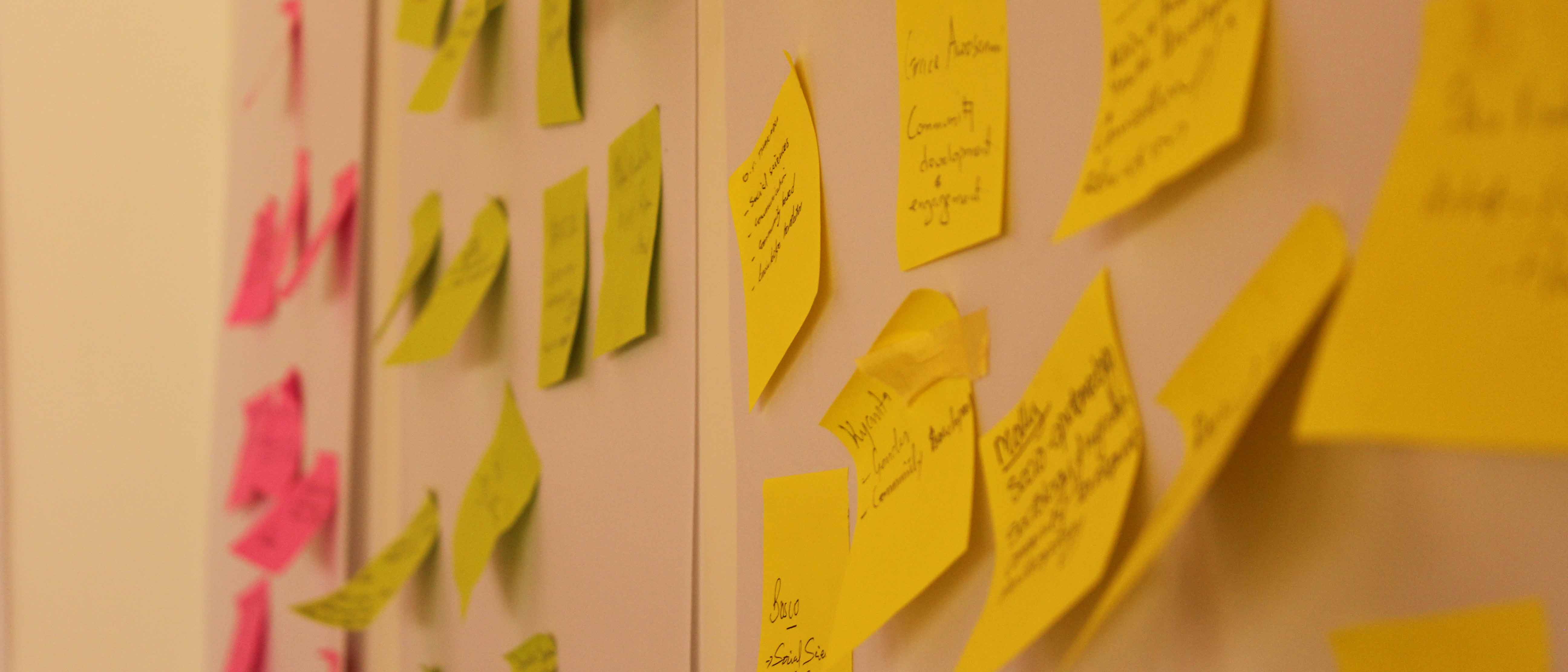 Post-It Notes in pink, green and yellow with writing on them stuck to a wall