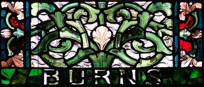 Burns' name on a stained glass pane white rose with green foliage