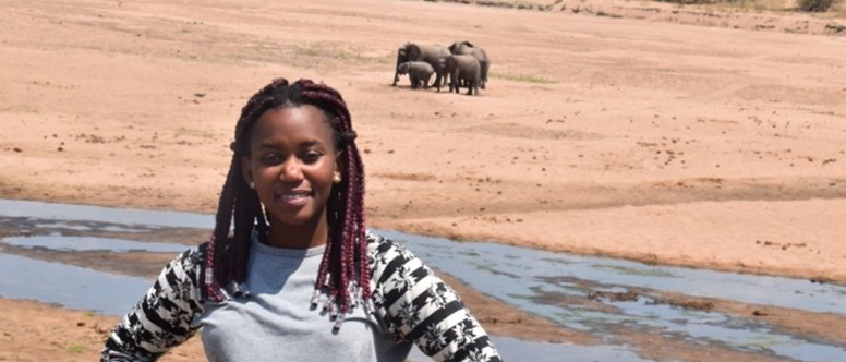 Young woman standing in the savanna with a group of elephants in the background