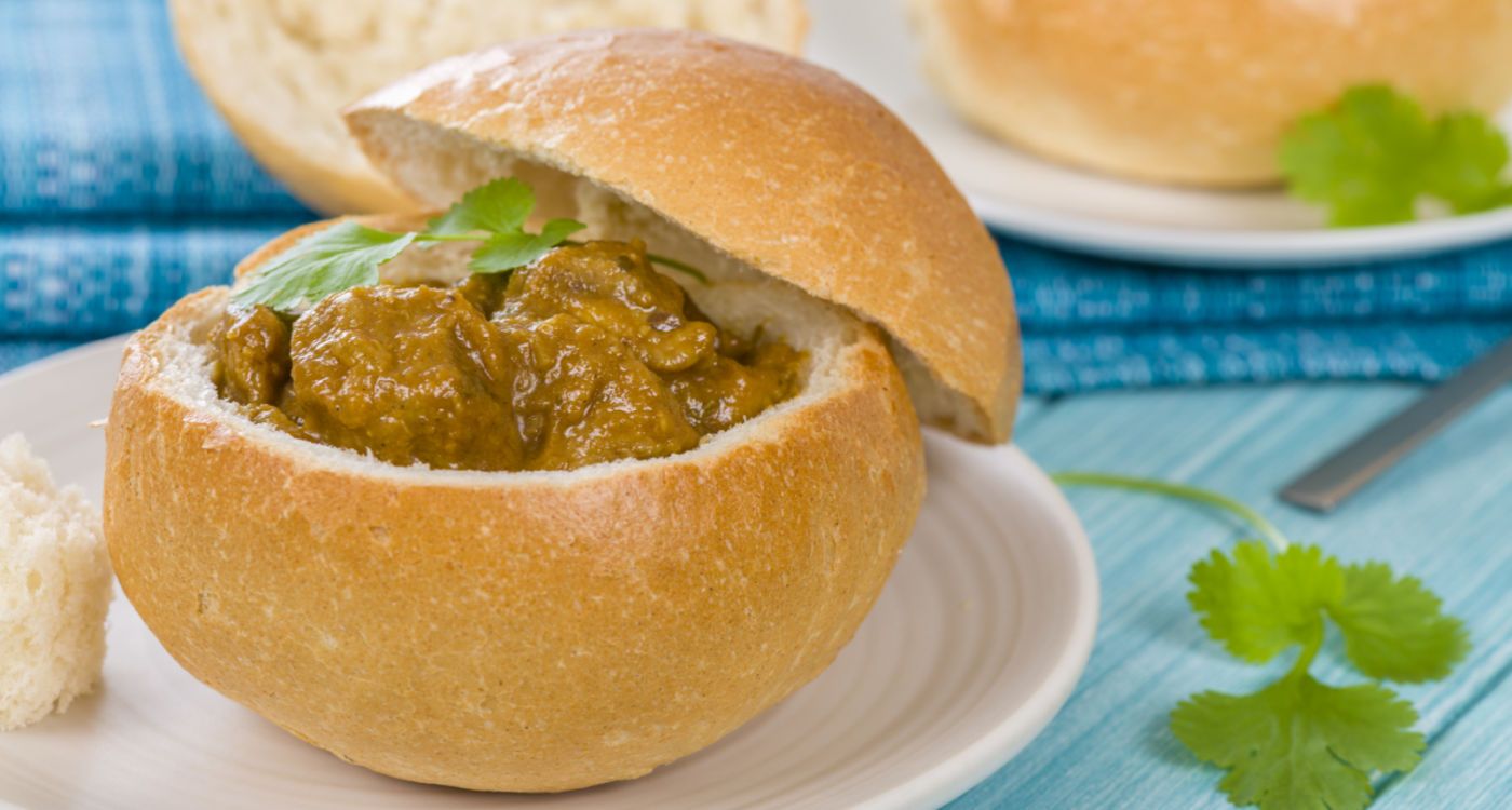 Two bunny chows (hollowed-out bread roll filled with curry) dished up on a plate [Photo: Shutterstock]