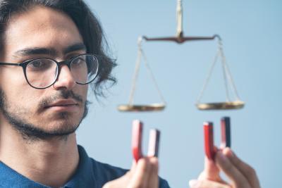 Portrait of young adult man holding u magnets and trying to balance scale of justice. Shot in close up with a full frame mirrorless camera.