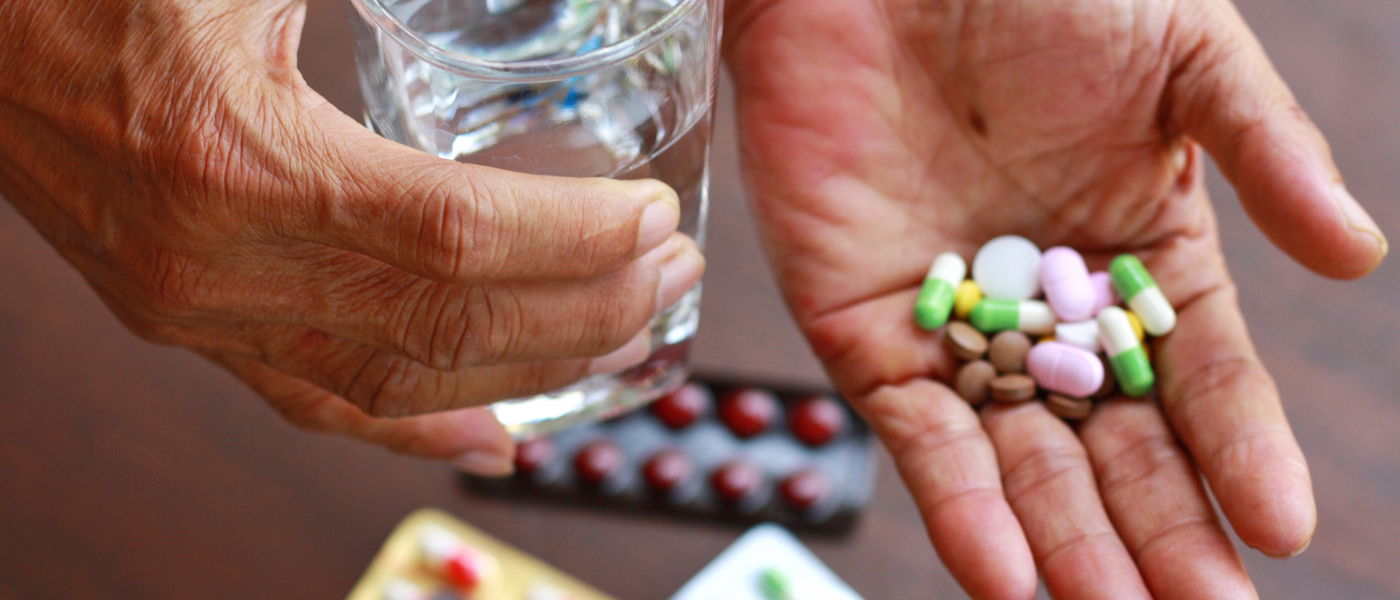 Photo of person taking a handful of medication with glass of water