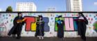 Four students wearing graduation gowns stand by a brightly coloured wall with a sign saying The Hub. They children are involved in the launch of IntoUniversity Maryhill centre 