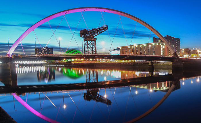 Beautiful Sunset Clyde Arc Bridge across river in Glasgow, Scotland, UK. It is nice weather with reflection on water, blue sky, lights from buildings in downtown, skyline, attractions.