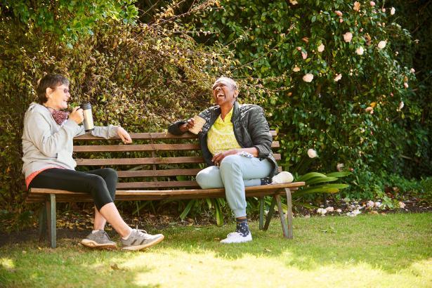 Two women sitting on a bench drinking coffee and laughing