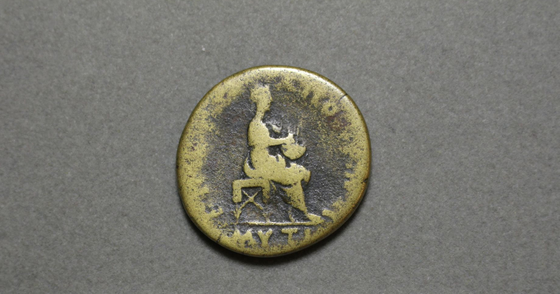 A bronze coin decorated with an image of a seated women playing a Lyre.  
