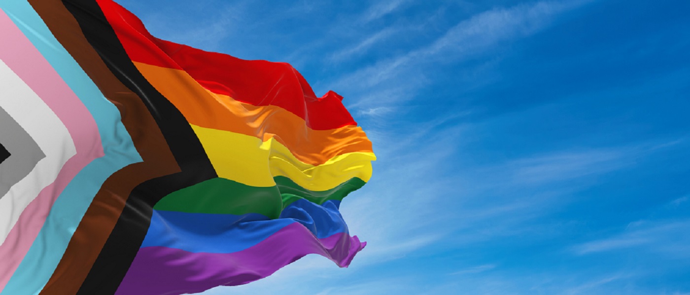 Photo of progressive pride flag against a clear blue sky