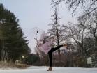 Angela Weihan balancing on one leg with umbrella raised in the air in the snow at Seoul National University Campus
