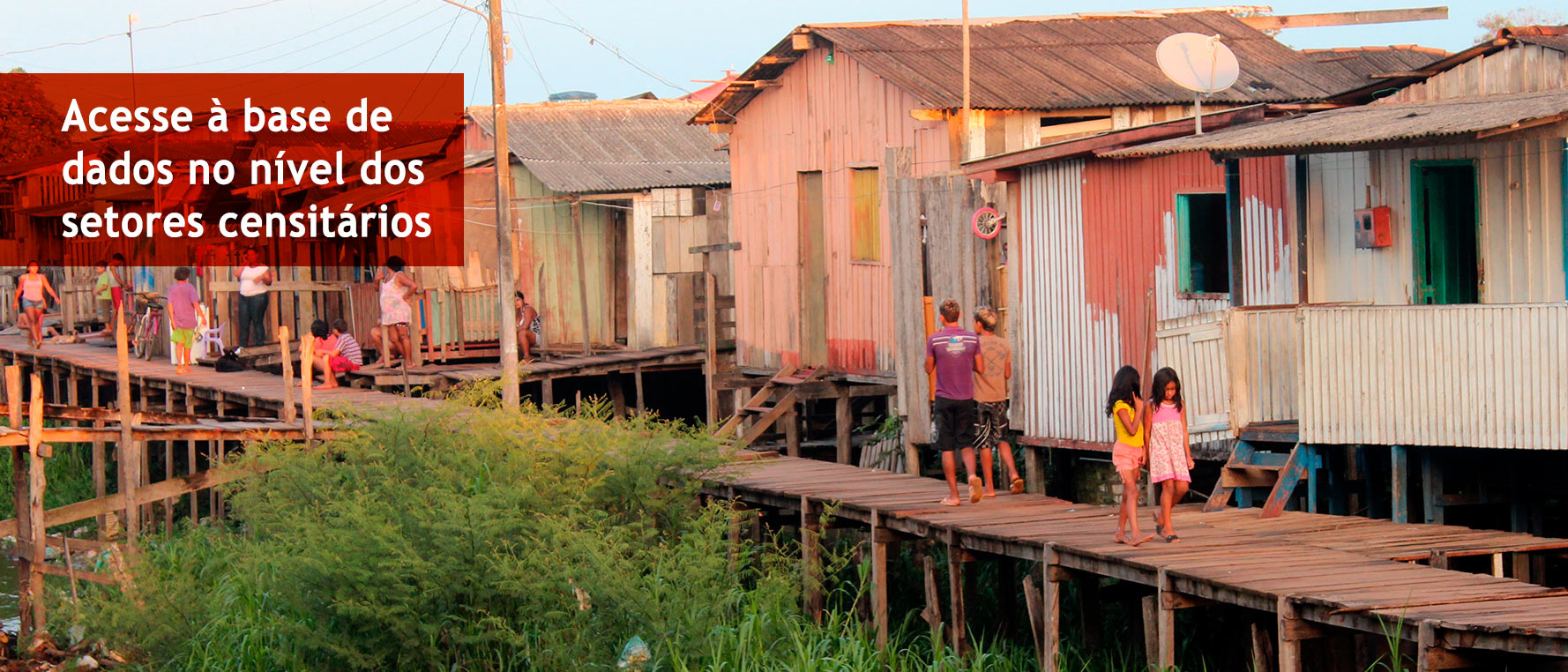 Two children walk on an elevated wooden boardwalk in front of buildings constructed from wood and corrugated metal