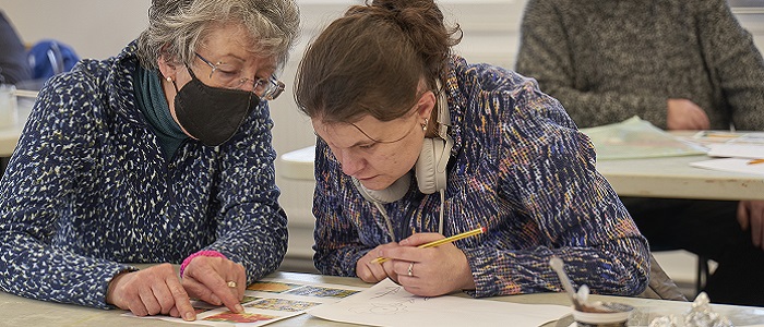 A young woman getting help in an art class and focused on her work. The instructor wears a COVID-19 facemask. Source: Centre for Aging Better https://ageingbetter.resourcespace.com/pages/view.php?ref=10997&k=&search=11883%2C+%40%40339&offset=0&order_by=&sort=DESC&archive=