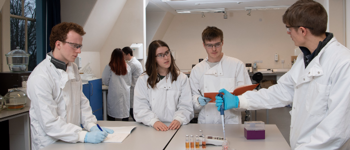 Three life sciences students in the lab being taught by a lecturer