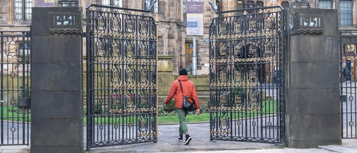 A student walking through the memorial gates at the University of Glasgow Main Building