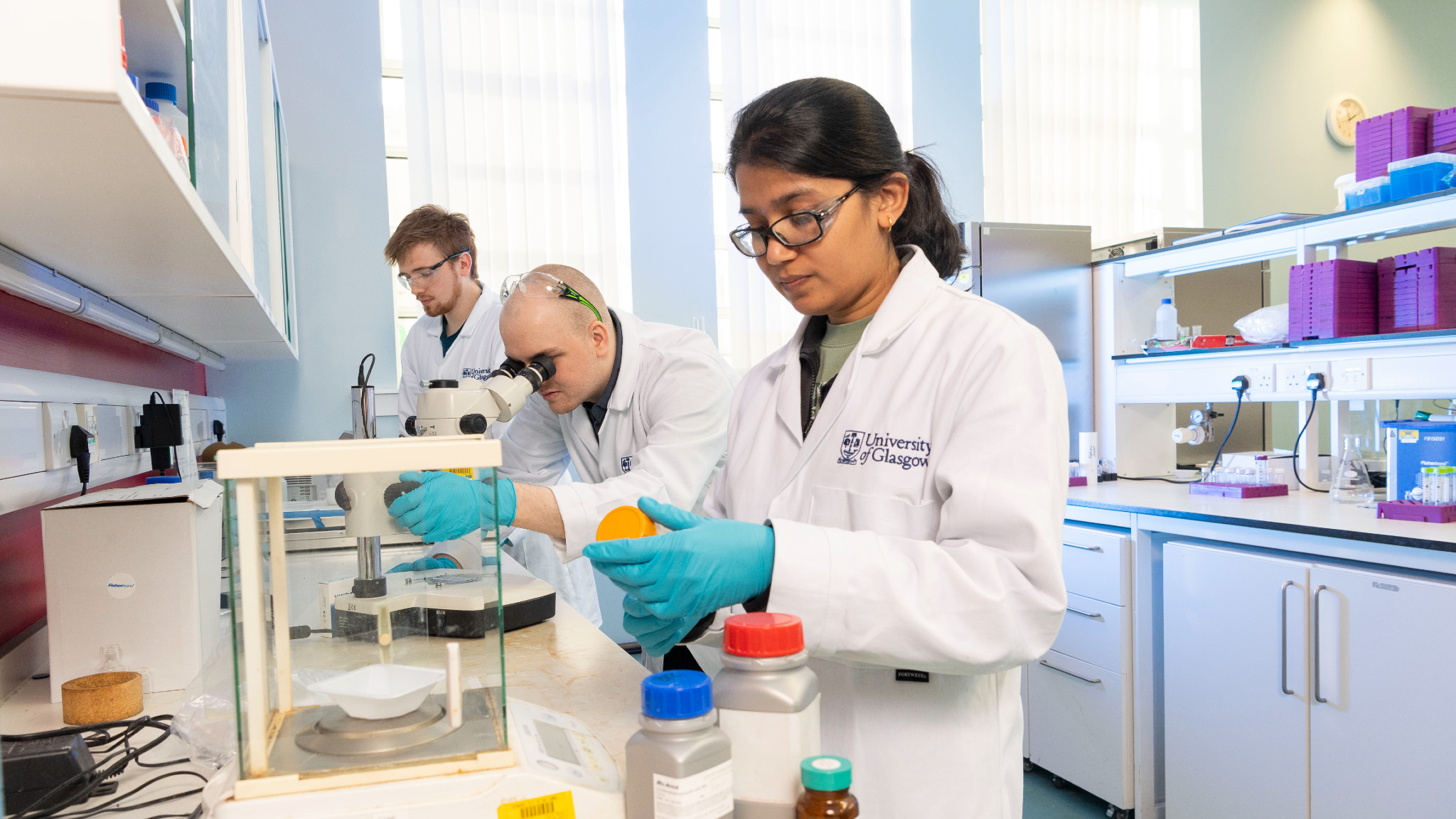 An image showing three students working in the lab, wearing UofG lab coats