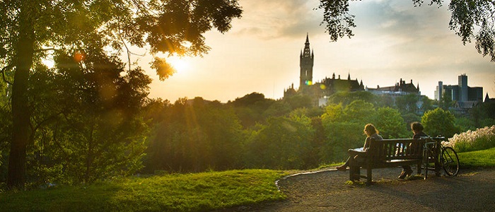 Two people reading while sitting on a park bench with the University's gothic tower in the distance in front of them is silhouetted against the sunset: Source: GU Image Library