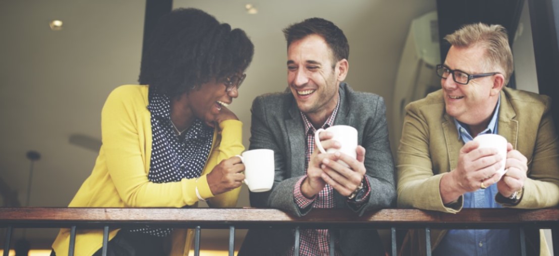 Three people standing leaning over a banister holding coffee and chatting