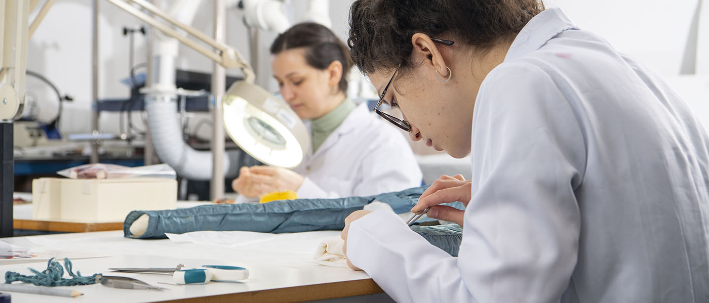 Two students wearing lab coats inspecting pieces of fabric