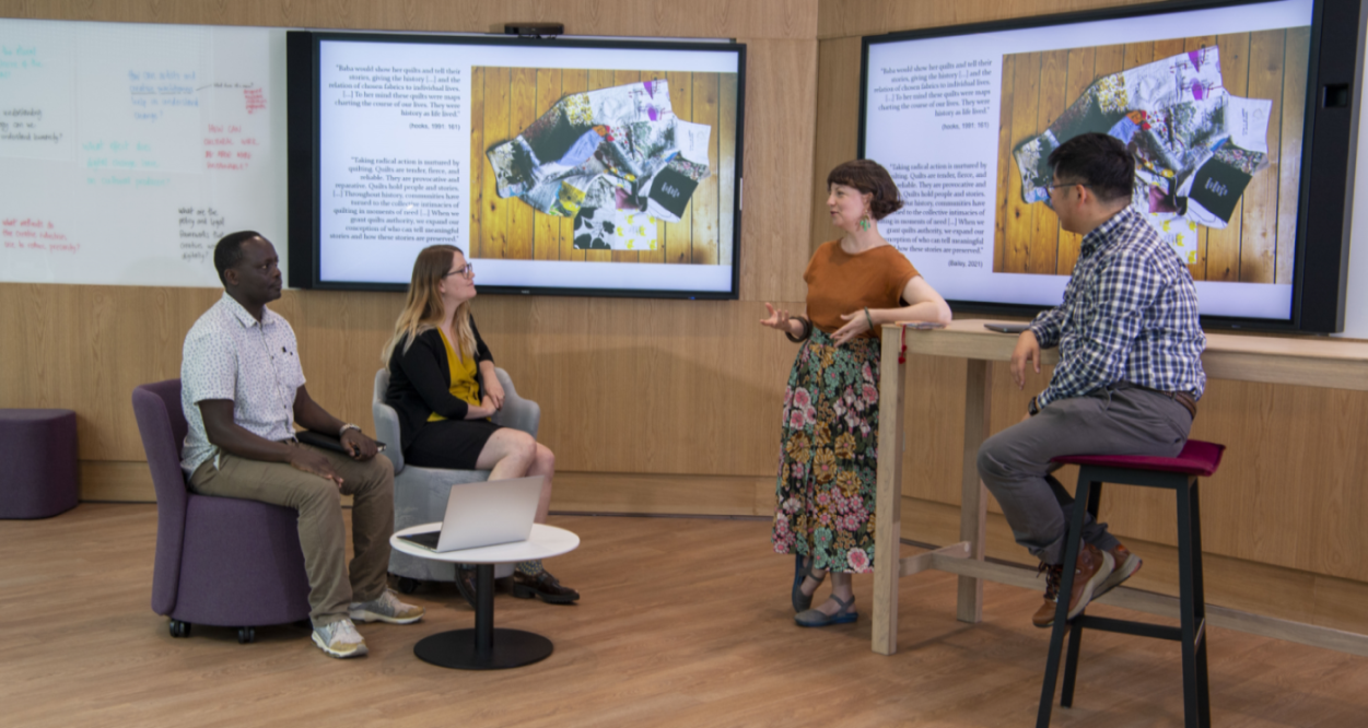 Four colleagues discussing and collaborating with two large screens behind them at the ARC building - image to showcase collaborative working at the university