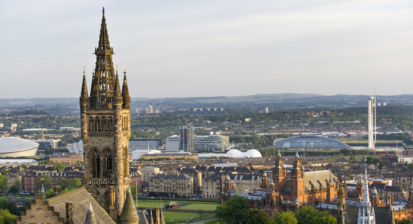 A view of the Glasgow University tower with the city visible beyond with green spaces, modern buildings, old buildings, tower blocks and hills in he background: Source: GU image library