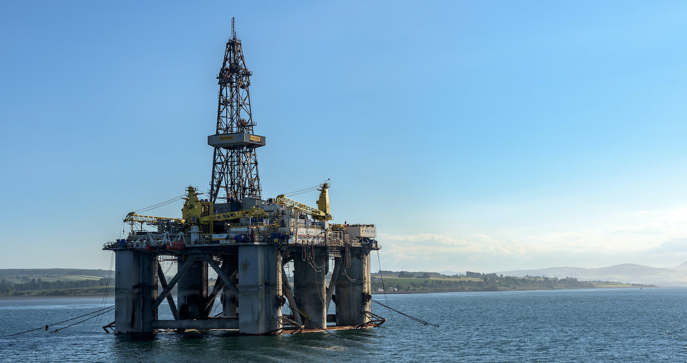 An oilrig platform standing in the sea with some land behind it Source: Mustang Joe, https://www.flickr.com/photos/mustangjoe/43258021631