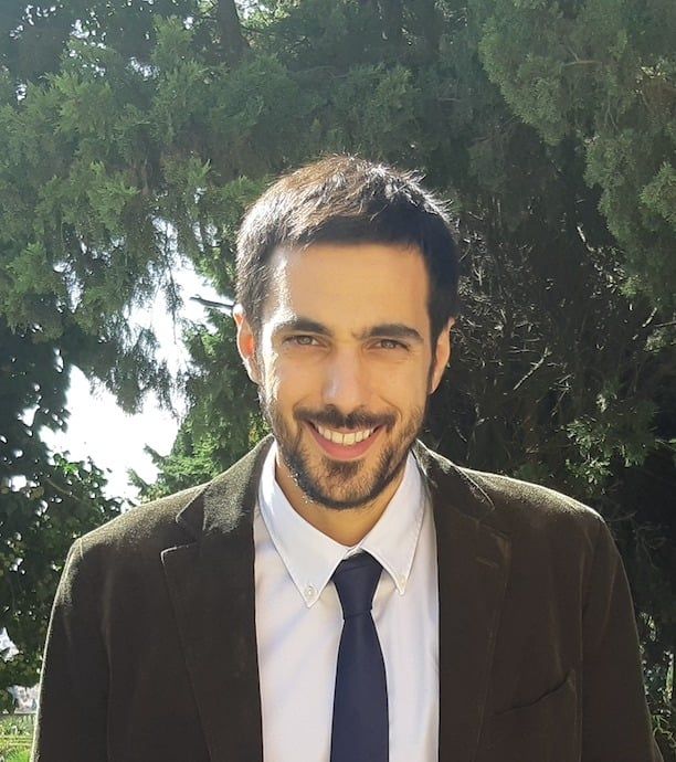 A young man in a suit in front of trees