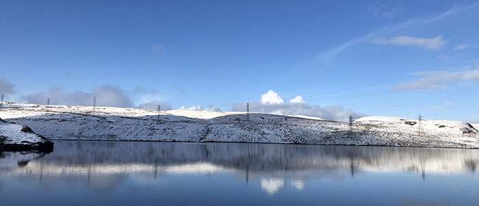 clear blue sky over a snowy strip of land above a smooth reflective lake surface